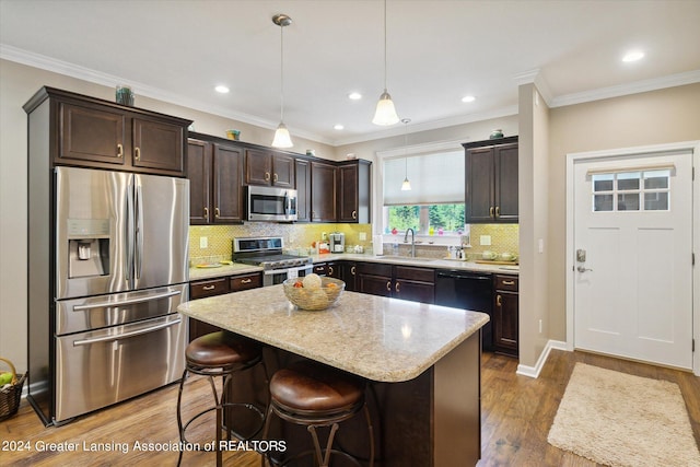 kitchen with hanging light fixtures, ornamental molding, appliances with stainless steel finishes, a kitchen island, and wood-type flooring