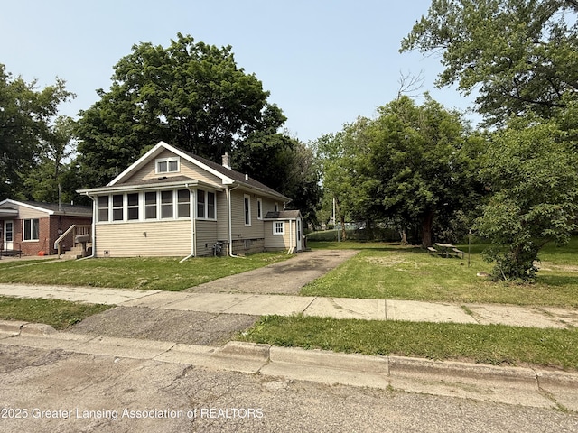 1555 Roosevelt Ave, Lansing, MI 48915 - view of front facade featuring concrete driveway, a front yard, a chimney, and view of wooded area