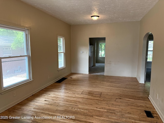 1555 Roosevelt Ave, Lansing, MI 48915 - unfurnished room featuring arched walkways, healthy amount of natural light, a textured ceiling, and wood finished floors