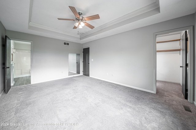 unfurnished bedroom with crown molding, ceiling fan, a raised ceiling, carpet flooring, and a spacious closet