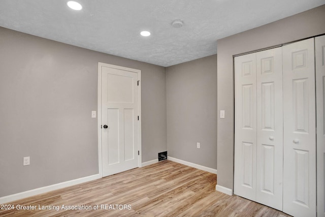 unfurnished bedroom with a textured ceiling, light hardwood / wood-style flooring, and a closet