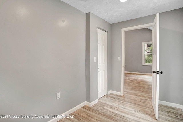 hallway with light wood-type flooring and a textured ceiling