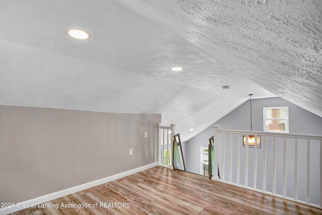 bonus room featuring an inviting chandelier, a textured ceiling, lofted ceiling, and hardwood / wood-style floors