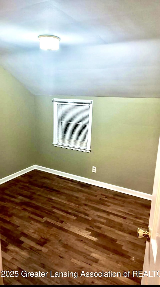 spare room featuring baseboards, wood finished floors, and vaulted ceiling