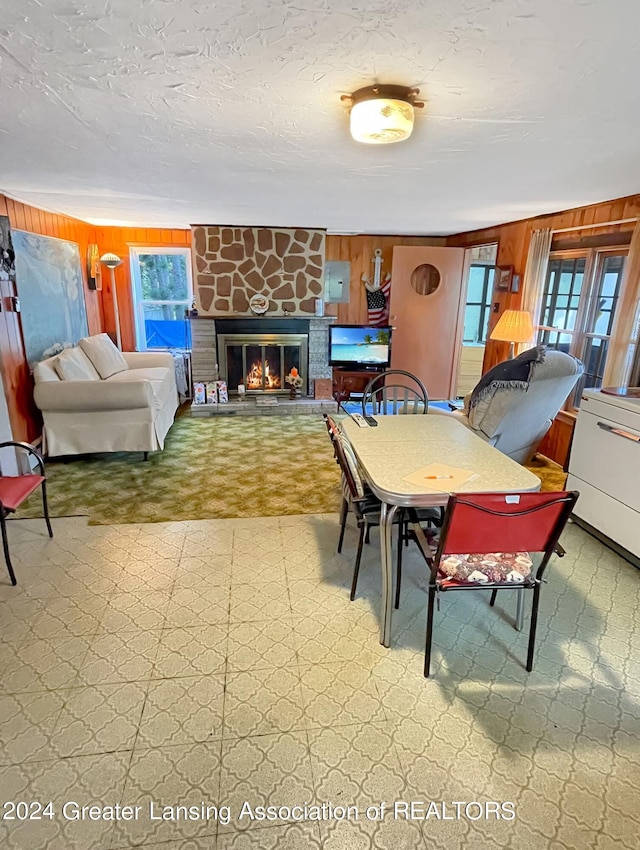 dining area featuring a stone fireplace and wood walls