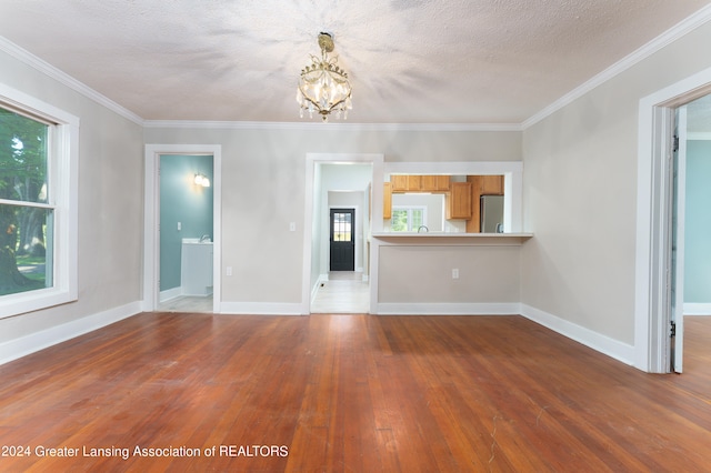 unfurnished living room with an inviting chandelier, ornamental molding, hardwood / wood-style floors, and a textured ceiling