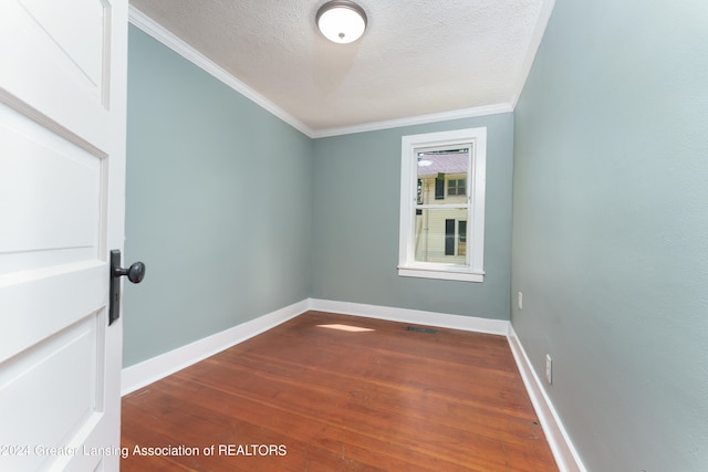 empty room featuring dark wood-type flooring, ornamental molding, and a textured ceiling