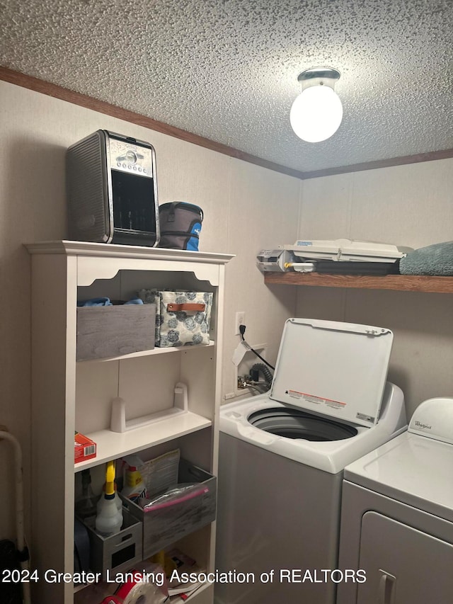 clothes washing area with washer and clothes dryer, a textured ceiling, and ornamental molding