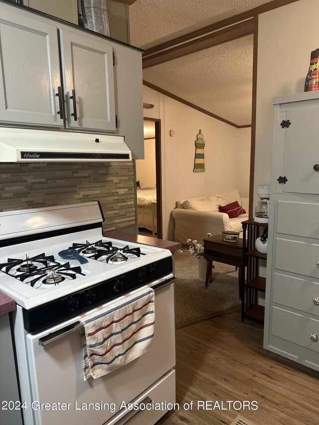 kitchen featuring hardwood / wood-style floors, decorative backsplash, a textured ceiling, white cabinetry, and white gas stove