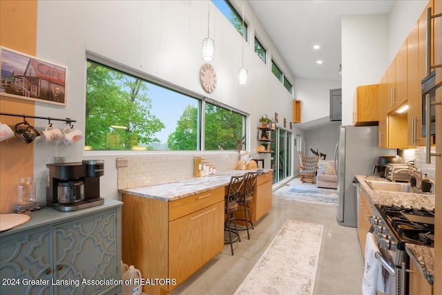 kitchen with sink, appliances with stainless steel finishes, hanging light fixtures, light stone counters, and decorative backsplash