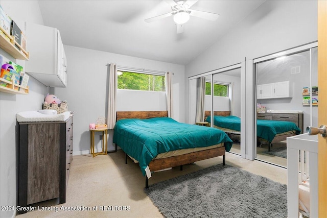 bedroom featuring lofted ceiling, ceiling fan, light carpet, and multiple closets