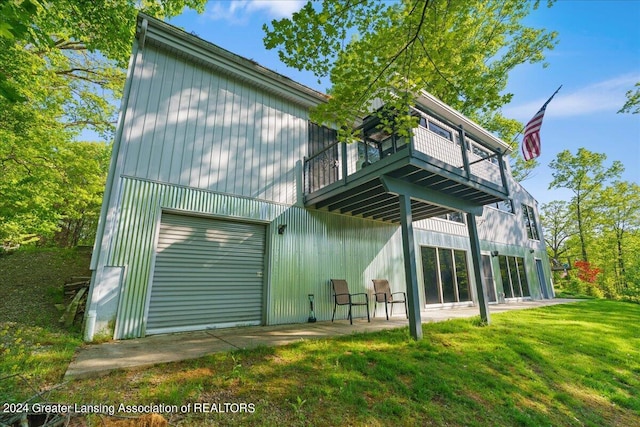 back of property with a garage, a balcony, and a lawn