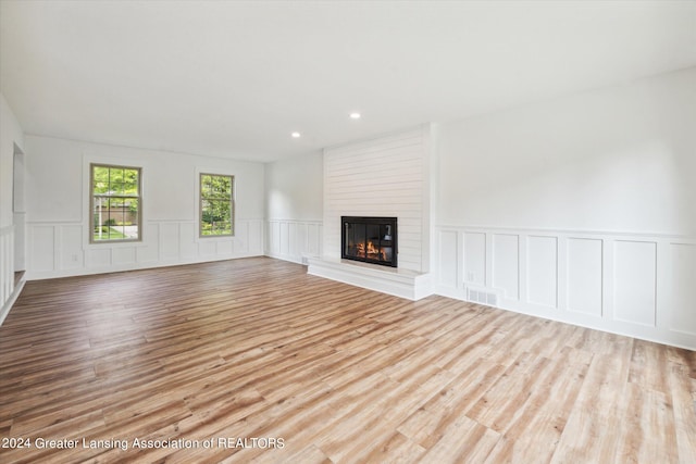 unfurnished living room with brick wall, light wood-type flooring, and a large fireplace