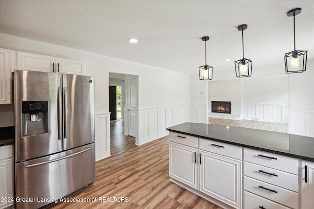 kitchen featuring a fireplace, hanging light fixtures, stainless steel refrigerator with ice dispenser, white cabinets, and light hardwood / wood-style flooring