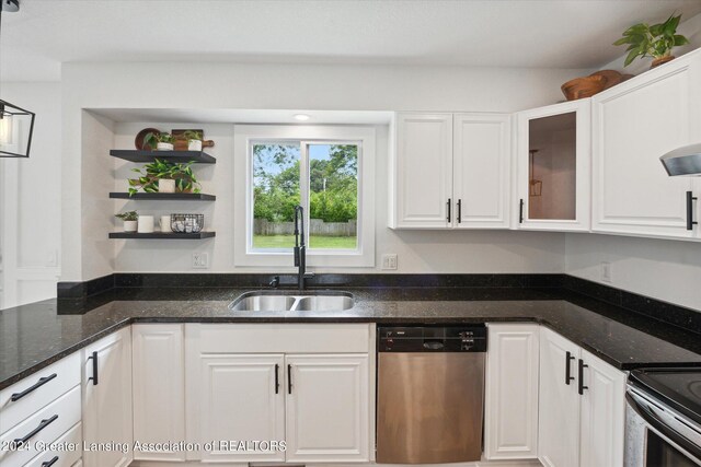 kitchen featuring stainless steel dishwasher, white cabinetry, range, sink, and dark stone countertops