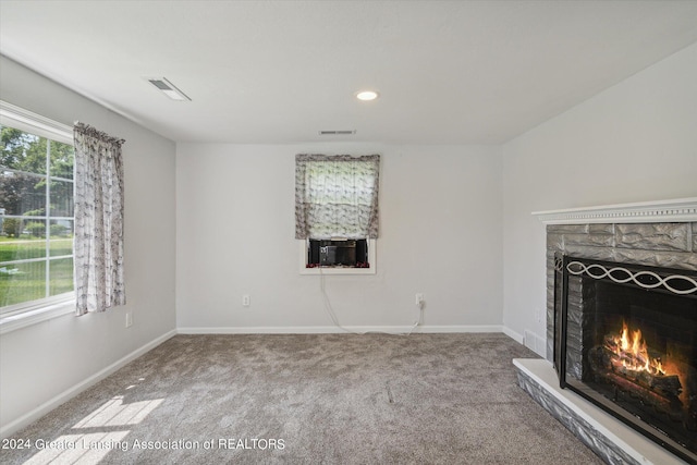 unfurnished living room with carpet, visible vents, a stone fireplace, and baseboards