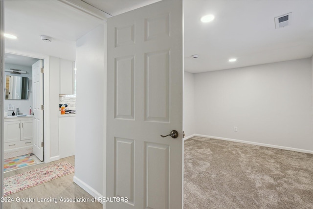 corridor featuring light carpet, baseboards, visible vents, and a sink