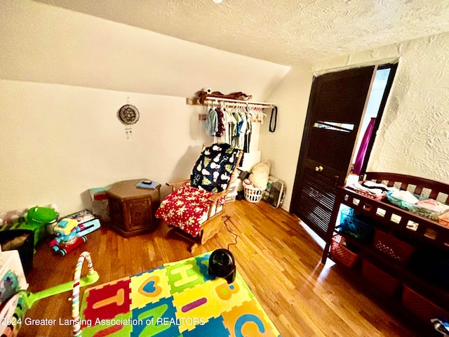 game room featuring wood-type flooring, vaulted ceiling, and a textured ceiling