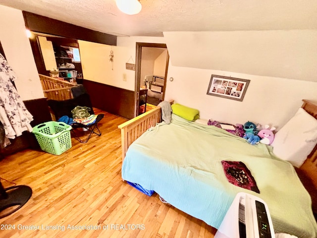 bedroom featuring vaulted ceiling, hardwood / wood-style flooring, and a textured ceiling