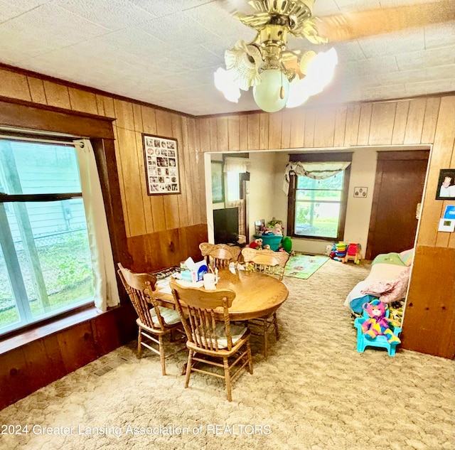 dining area with plenty of natural light, ceiling fan, wood walls, and carpet floors