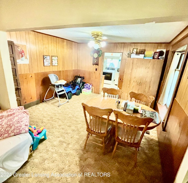 dining space featuring wood walls, ceiling fan, and carpet floors