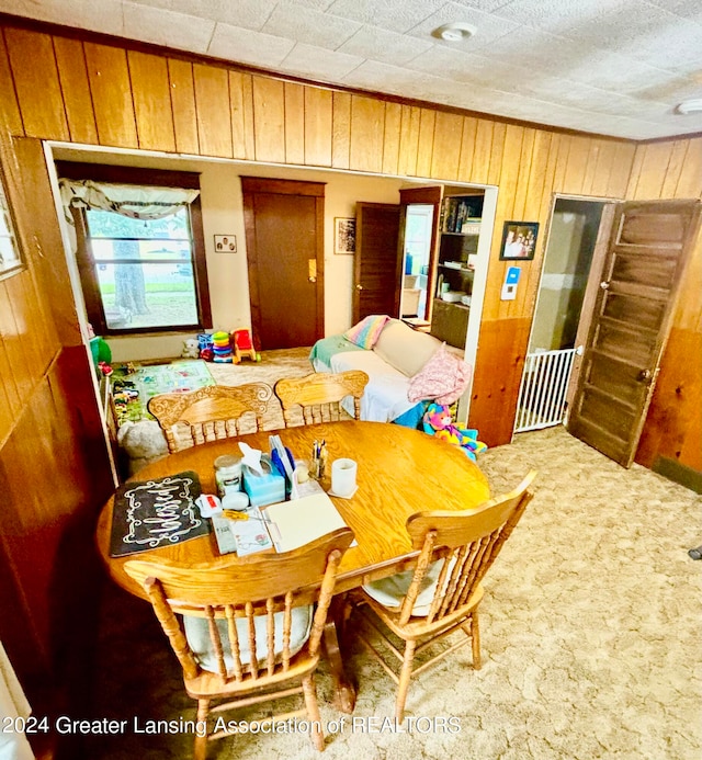 carpeted dining space featuring wood walls