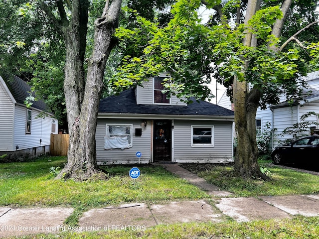 view of front facade featuring a front yard, fence, and roof with shingles