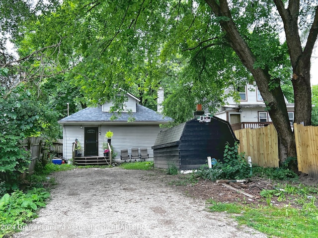 view of front of property with a storage shed, roof with shingles, fence, and an outbuilding