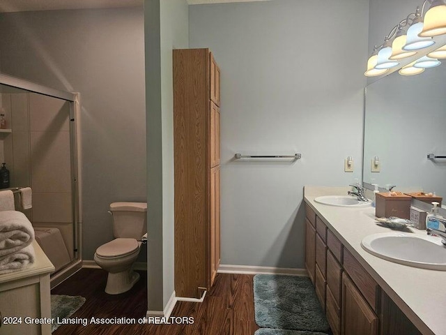 bathroom with a shower with shower door, hardwood / wood-style flooring, double sink vanity, and toilet