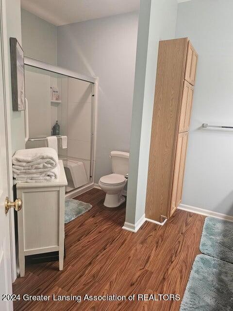 bathroom featuring an enclosed shower, wood-type flooring, and toilet