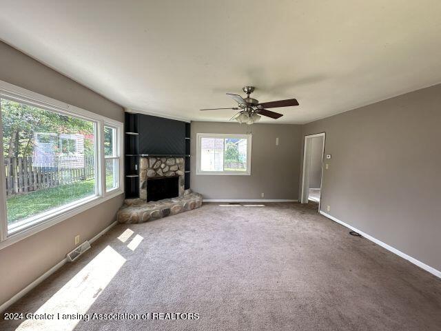 unfurnished living room with carpet floors, a fireplace, visible vents, ceiling fan, and baseboards