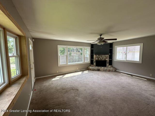 unfurnished living room featuring carpet floors, a fireplace, a ceiling fan, and baseboards