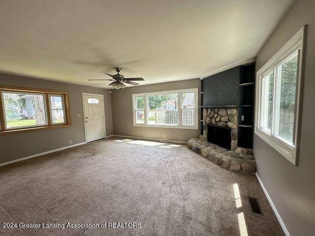 unfurnished living room with visible vents, baseboards, ceiling fan, carpet flooring, and a stone fireplace