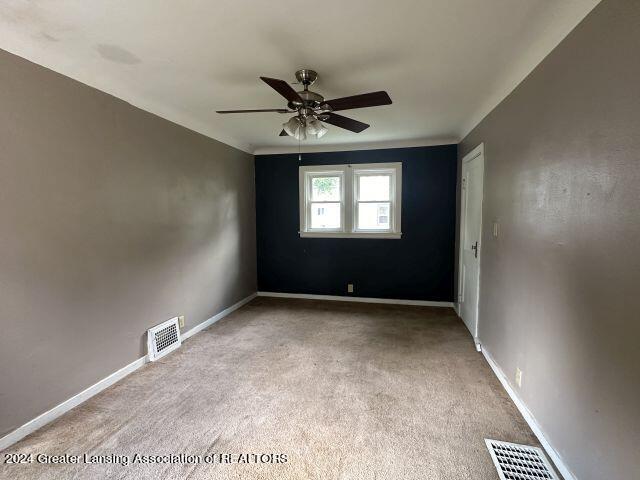 carpeted spare room featuring baseboards, visible vents, and a ceiling fan