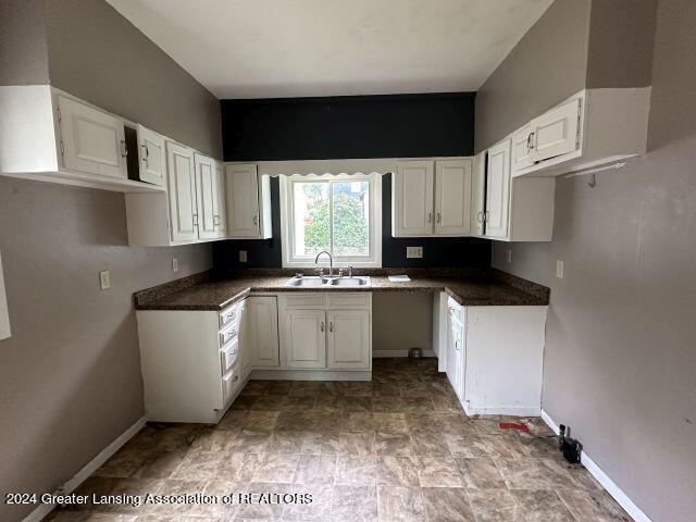 kitchen with dark countertops, baseboards, white cabinets, and a sink