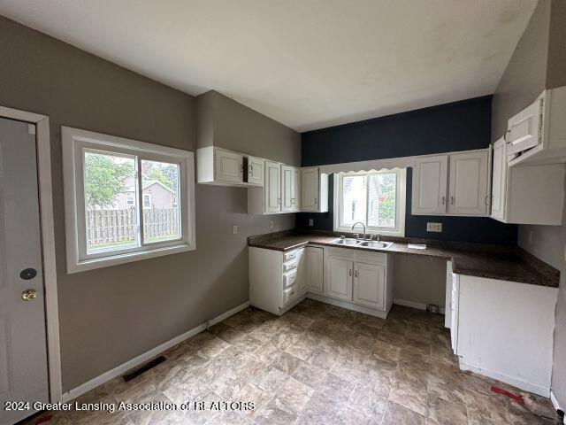 kitchen with dark countertops, visible vents, white cabinets, a sink, and baseboards