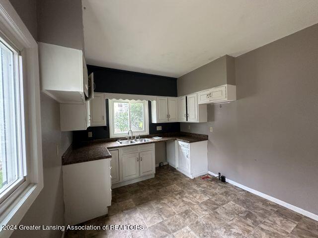 kitchen with dark countertops, white cabinetry, baseboards, and a sink