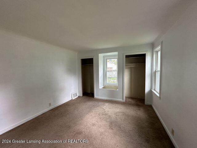 unfurnished bedroom featuring baseboards, carpet, visible vents, and two closets