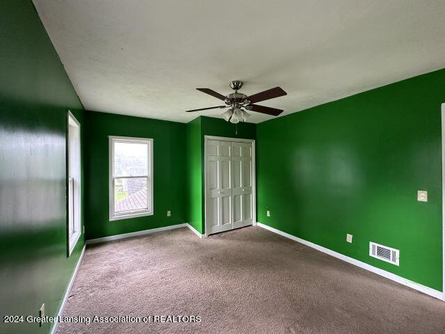 unfurnished bedroom featuring carpet floors, a ceiling fan, visible vents, baseboards, and a closet