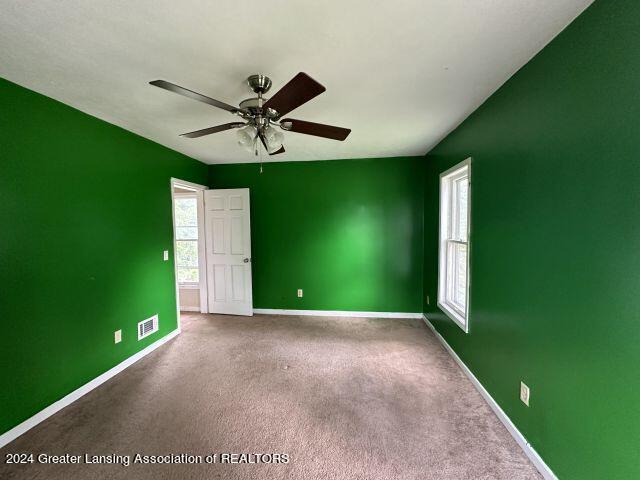 carpeted empty room with visible vents, plenty of natural light, baseboards, and ceiling fan