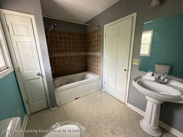 bathroom featuring a combined bath / shower with jetted tub, a textured ceiling, and baseboards