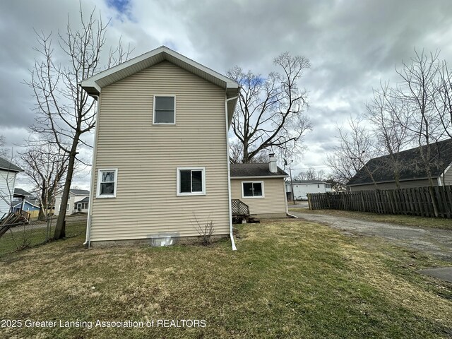 rear view of house with a chimney, fence, and a yard