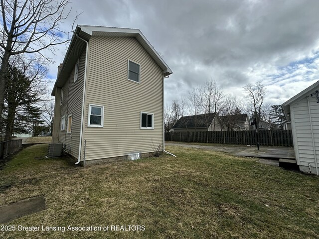 view of side of home featuring fence, central AC unit, and a yard