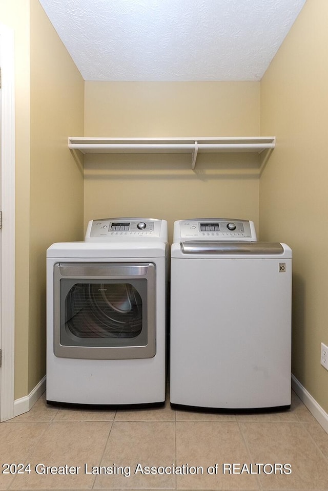 laundry area featuring a textured ceiling, washing machine and dryer, and light tile patterned floors