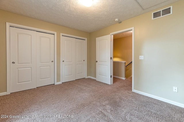 unfurnished bedroom featuring light carpet, two closets, and a textured ceiling