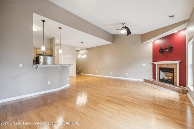 unfurnished living room featuring light hardwood / wood-style floors, ceiling fan with notable chandelier, and a tiled fireplace