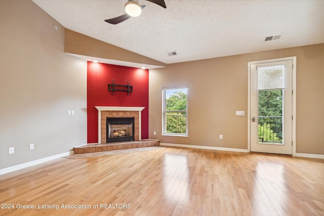 unfurnished living room featuring ceiling fan, light wood-type flooring, a fireplace, a textured ceiling, and lofted ceiling