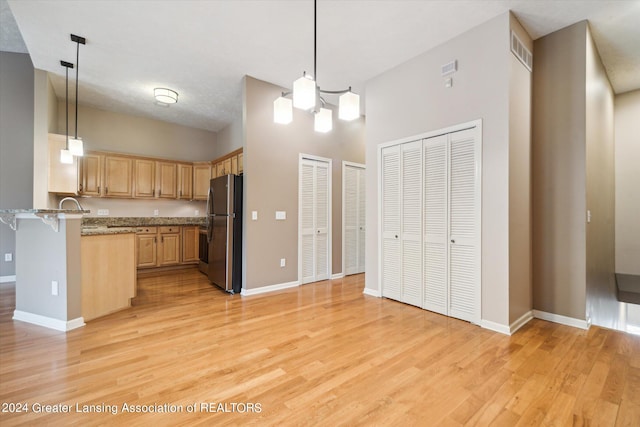 kitchen with light brown cabinets, light hardwood / wood-style flooring, hanging light fixtures, a towering ceiling, and stainless steel refrigerator