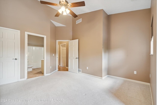 unfurnished bedroom featuring ceiling fan, a high ceiling, light colored carpet, and ensuite bath