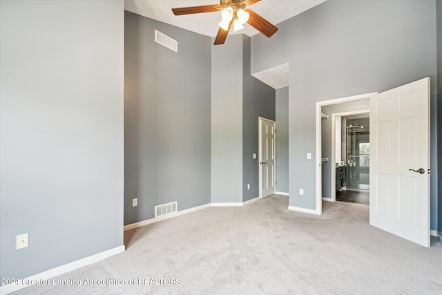 unfurnished bedroom featuring ceiling fan, a towering ceiling, and light colored carpet